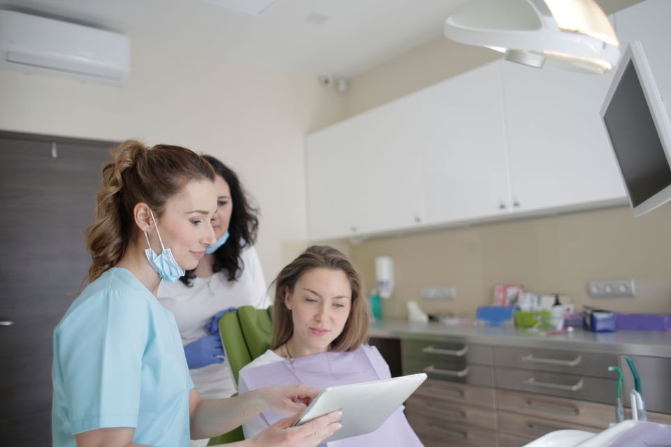 A dental professional reviewing a tablet with a patient seated in a dental chair.